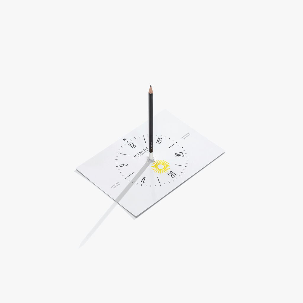 Tarjeta de reloj solar A5 con instrucciones en el reverso y un lápiz negro. Solo tiene que sostener la tarjeta con la «N» apuntando al norte, pasar el lápiz por la marca en relieve y leer la hora local a partir de la sombra del lápiz.